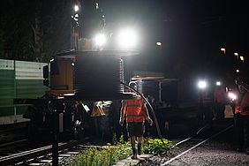 Mitarbeiter der DB Netz AG führen nachts Arbeiten an der Leit- und Sicherungstechnik durch. Schienwerfer leuchten die Baustelle aus. 