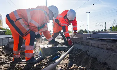 Das Symboldbild zeigt zwei Männer mit Bauhelm und orangefarbener Arbeitskleidung bei einer Baumaßnhme der DB InfraGO
