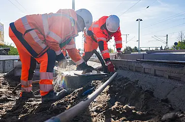 Das Symboldbild zeigt zwei Männer mit Bauhelm und orangefarbener Arbeitskleidung bei einer Baumaßnhme der DB InfraGO