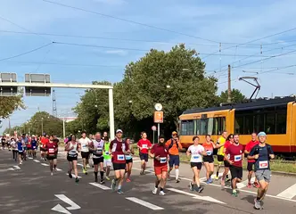 Das Foto zeigt Teilnehmer*innen des Baden-Marathons, die entlang der Durlacher Allee laufen. Im Hintergrund fährt eine Bahn vorbei.