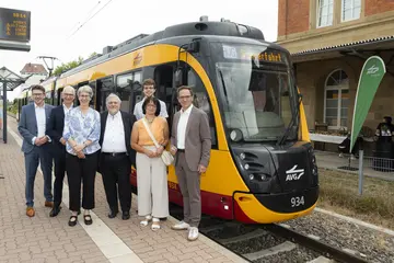 Politische Vertreter und Geschäftsführer stehen vor einer Stadtbahn am Bahnsteig.