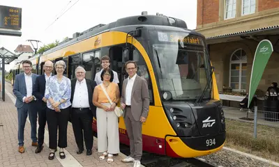 Politische Vertreter und Geschäftsführer stehen vor einer Stadtbahn am Bahnsteig.