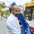 Mann mit einem Kontrabass-Case steht an der Haltestelle mit einer Bahn
