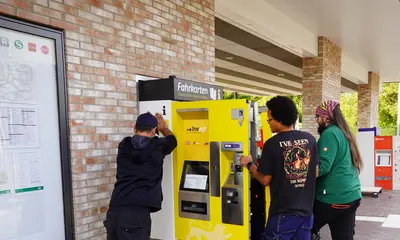 Drei Männer hieven einen neuen gelb-weißen Fahrscheinautomaten in eine Aussparung in einer Mauer am Bahnsteig der Haltestelle Böckingen Sonnenbrunnen