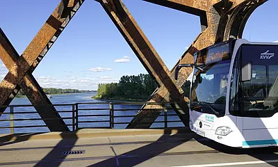 Ein silber-farbener Bus fährt über die Wintersdorfer Brücke bei Rastatt-Wintersdorf. Im Hintergrund sieht man den Rhein. 
