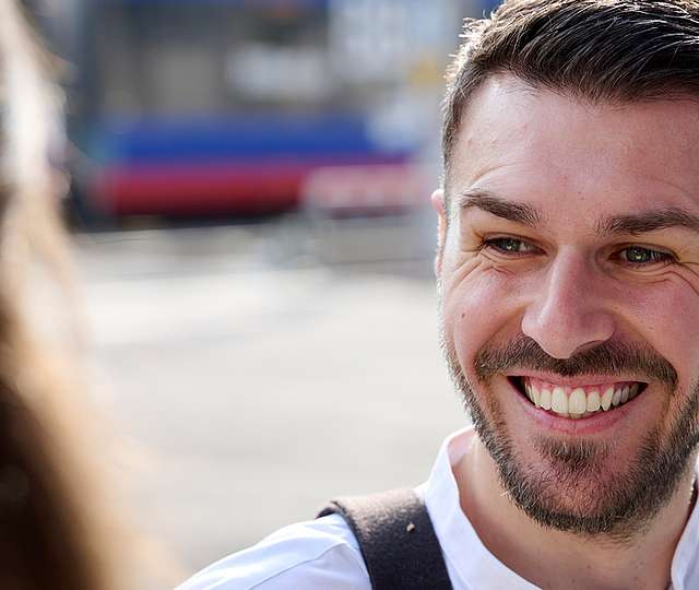 Ein junger Mann steht lächelnd an einer Haltestelle und unterhält sich.