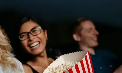 Eine Frau sitzt im Kino, isst Popcorn und lacht. 