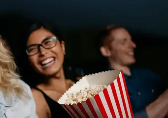 Eine Frau sitzt im Kino, isst Popcorn und lacht. 