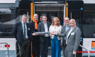 Eine Gruppe von Menschen steht vor einer Tür des VDV-TramTrain mit einem Modell der Bahn.