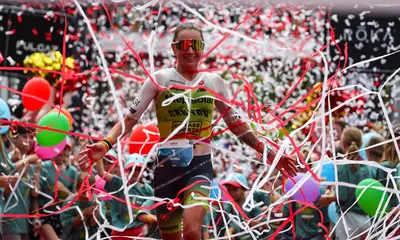 Eine Sportlerin überquert die Ziellinie beim Ironman Kraichgau. Luftschlangen wirbeln durch die Luft.