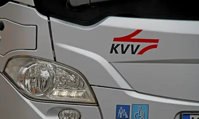 Über dem Scheinwerfer eines silberfarbenen Busses steht das KVV-Logo. 