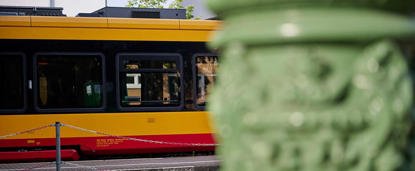 Im Hintergrund einer Säule hält eine KVV-Bahn an einer Haltestelle.