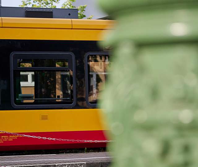 Im Hintergrund einer Säule hält eine KVV-Bahn an einer Haltestelle.