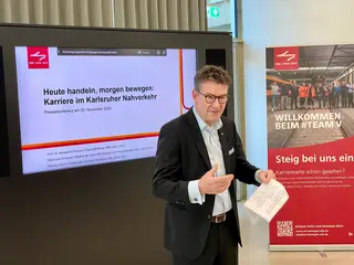 Prof. Dr. Alexander Pischon (Geschäftsführer von KVV, VBK und AVG) bei der Präsentation der neuen Karrierewebsite. Hinter ihm stehe ein großer Monitor.