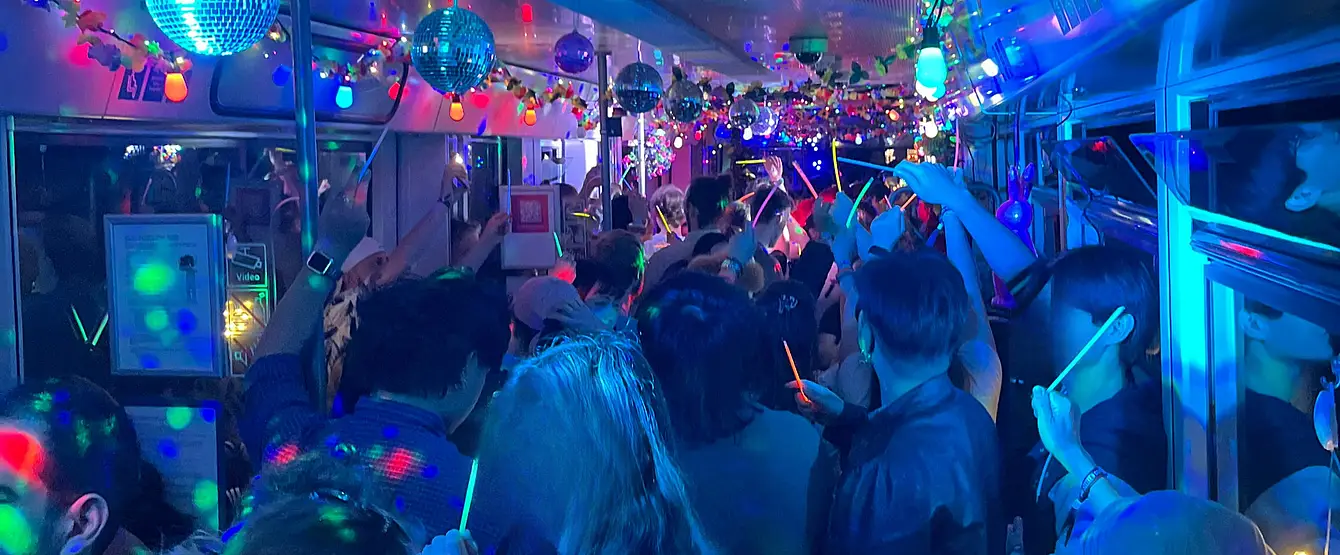 Partyatmosphäre mit bunten Lichtern in einer Bahn mit Menschen.