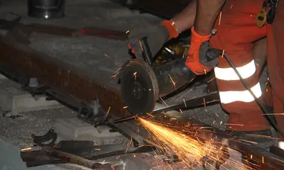 Das Symbolfoto zeigt nächtliche Gleisbauarbeiten. Eine Flex durchtrennt ein Metallstück, Funken sprühen.