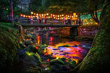 Fluss mit Brücke. Auf der Brücke hängen Lichtergirlanden.