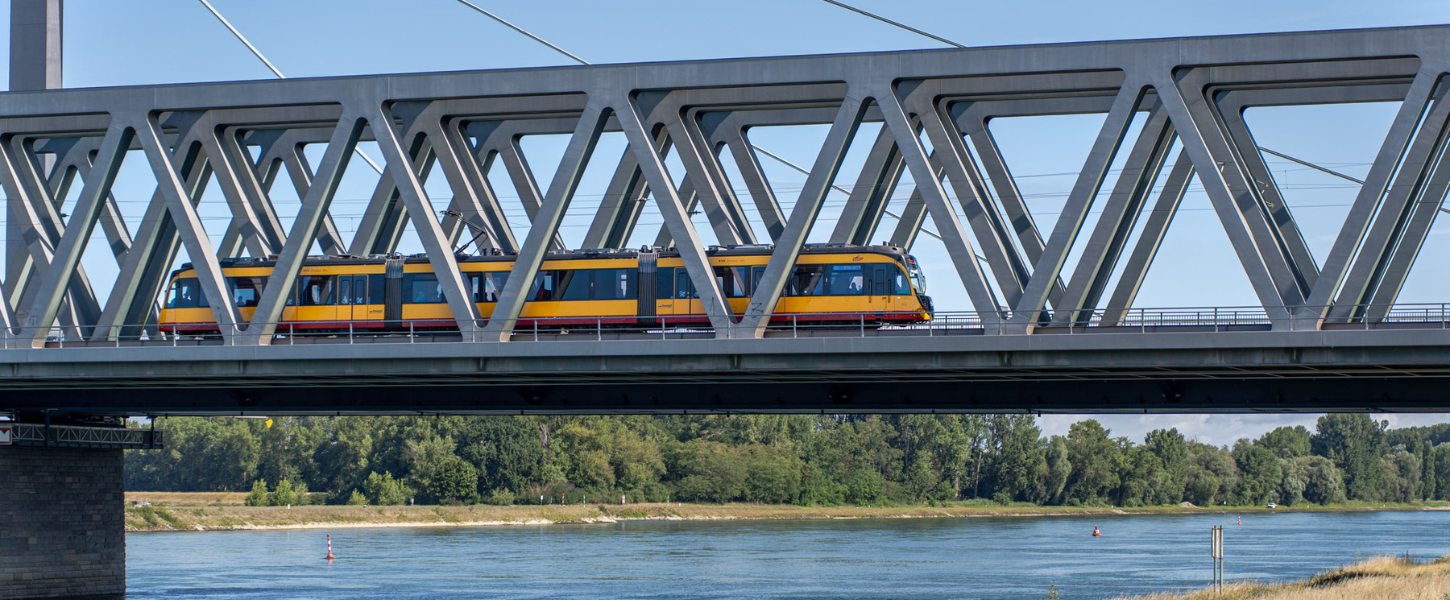 Eine gelbe AVG-Bahn fährt über die Rheinbrücke Richtung Südpfalz.