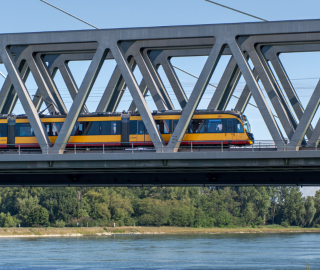 Eine gelbe AVG-Bahn fährt über die Rheinbrücke Richtung Südpfalz.