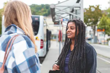 Zwei Mädchen unterhalten an einer Bushaltestelle.