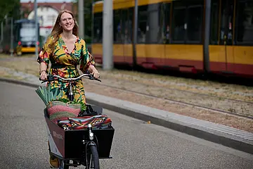 Eine Frau fährt auf einem Lastenrad von KVV.nextbike. Im Hintergrund ist eine Straßenbahn zu sehen.