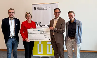 Das Foto zeigt die Übergabe des symbolischen Förderschecks durch Landes-Wirtschaftsministerin Dr. Nicole Hoffmeister-Kraut an die AVG.  