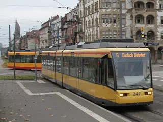 Eine Trambahn der Linie 5 hält am Bahnsteig der Haltestelle Tullastraße in Karlsruhe. Im Hintergrund sind Häuserfassaden zu sehen.