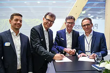 Auf der Innotrans in Berlin haben stehen Männer um einen Tisch. 