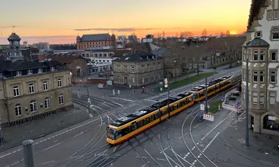 Blick von oben auf das Gleisviereck Schlachthof, Durlacher Allee und Tullastraße von schräg oben. Die untergehende Abendsonne taucht das Bild in eine dunkel-orangefarbene Lichtstimmung.