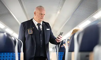 Ein Mitarbeiter des Prüfpersonals der Deutschen Bahn kontrolliert in einer Regionalbahn Fahrausweise. Dabei trägt er eine Bodycam.