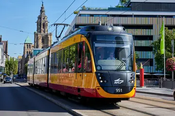 Eine AVG-Stadtbahn fährt durch die Heilbronner Innenstadt und überquert die Friedrich-Ebert-Brücke. Im Hintergrund ist ein Kirchturm der Stadtkirche zu sehen