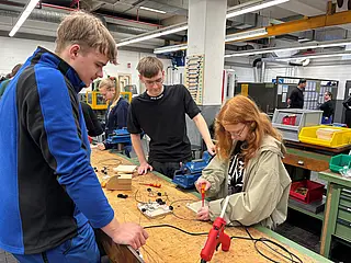 Mitarbeitende der Werkstatt im BHW zeigen einer Schülerin wie man eine Stromschaltung macht.