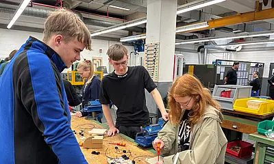 Mitarbeitende der Werkstatt im BHW zeigen einer Schülerin wie man eine Stromschaltung macht.