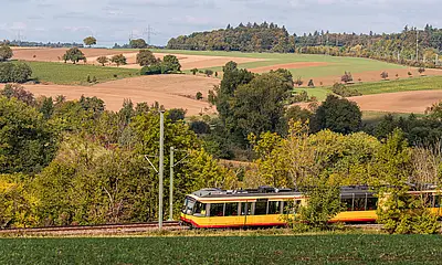 AVG-Stadtbahn fährt durch Landschaft in schöner Kulisse.