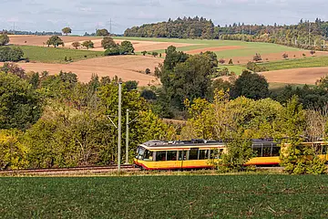 AVG-Stadtbahn fährt durch Landschaft in schöner Kulisse.