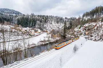 Eine AVG-Stadtbahn fährt durchs verschneite Murgtal.