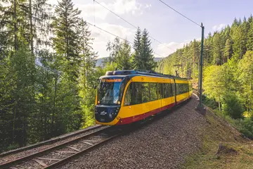 Ein gelbes Zweisystemfahrzeug der AVG fährt unter blauem Himmel im Murgtal.