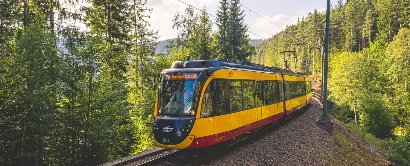 Ein gelbes Zweisystemfahrzeug der AVG fährt unter blauem Himmel im Murgtal.